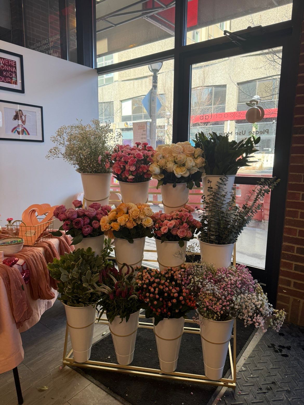 Gold Bloom Bar stand with pastel roses, eucalyptus and berries in a city storefront
