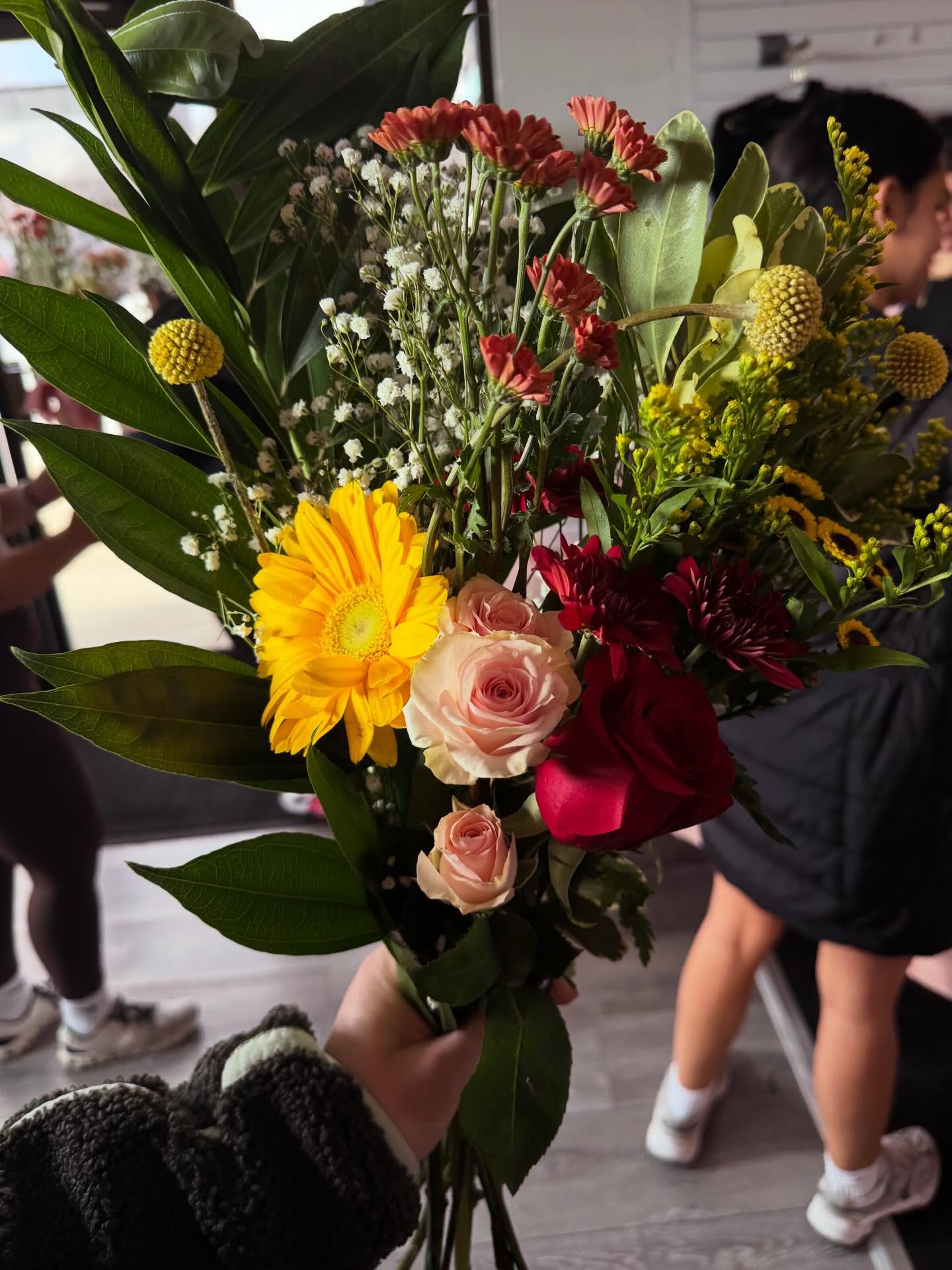 Hand holding a freshly built bouquet with roses, gerbera daisy and wildflowers