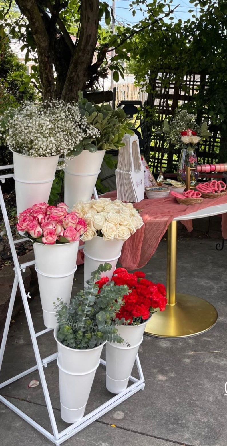 White Bloom Bar stand with roses and eucalyptus beside a gold table on a patio