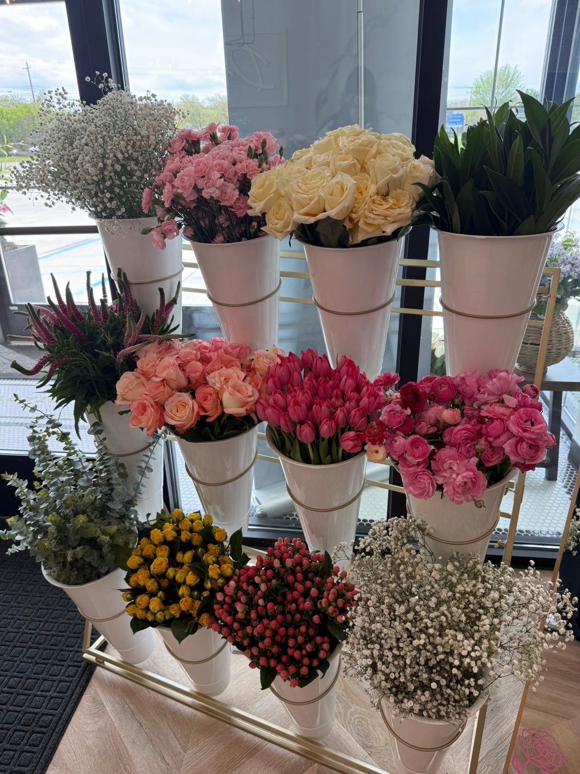 Gold Bloom Bar stand with pink tulips, ranunculus, roses and baby's breath by a sunny window