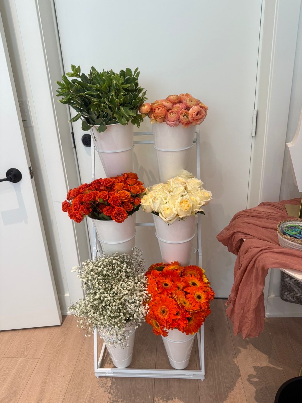 White flower stand with peach ranunculus, orange spray roses, gerbera daisies and baby's breath